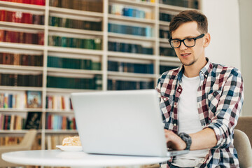 Young business man, uses laptop, man works on the internet sitting at a table with a modern laptop computer in a cafe