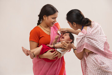A health officer giving polio drops to a baby in his mother's lap. - obrazy, fototapety, plakaty