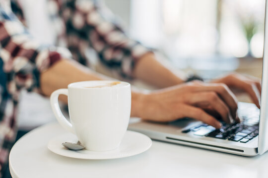 image of male hands working and typing on a laptop keyboard with a cup of coffee on a wooden table, Man working from home.