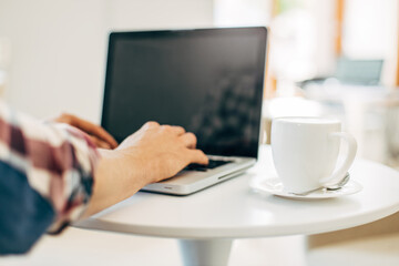 Fototapeta premium Man using laptop in cafe sitting on wooden table, male hands are typing on laptop keyboard