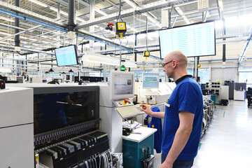 production and assembly of microelectronics in a hi-tech factory - man operates machine in production - obrazy, fototapety, plakaty
