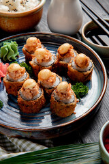 side view of baked sushi rolls with shrimps  ginger and wasabi on a plate served with soy sauce on wooden background