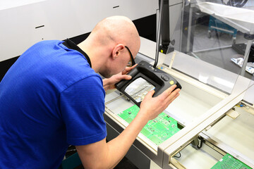 quality control in the production - man checks board for defects - manufacturing in a high tech...