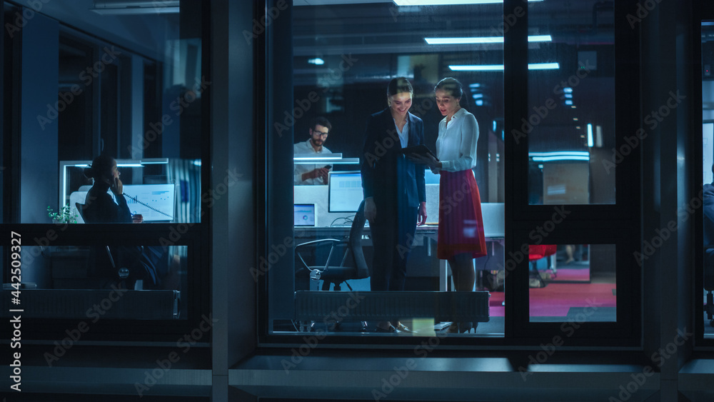 Aufkleber shot from outside: two businesswomen working on a tablet computer in office. managers standing by th