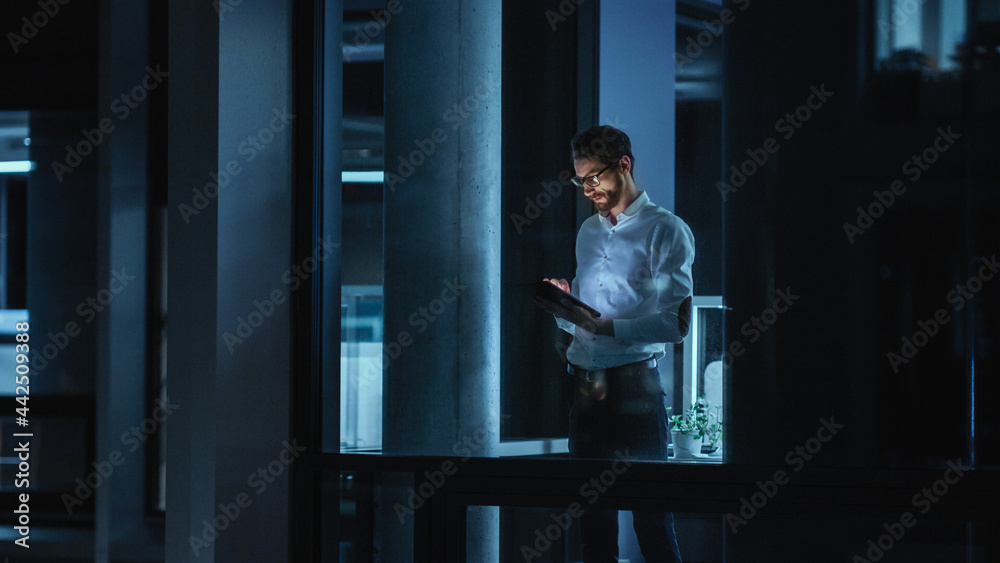 Poster Shot from Outside: Businessman Working on a Digital Tablet Computer in the Office. Manager Checking Emails while Standing by the Window. Employee Planning Financial Tasks and Business Development.