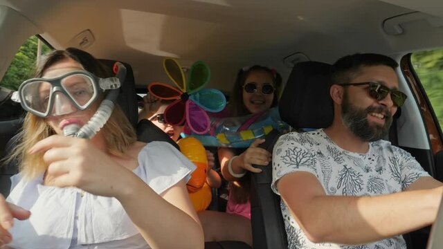A crazy funny family with children traveling in a car. Woman in diving mask with a snorkel, everyone is having fun and dancing, enjoying their vacation