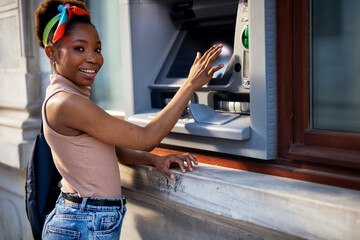 Beautiful african women using ATM machine. Attractive young woman withdrawing money from credit card at ATM..