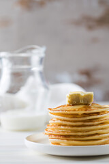 The pancakes are stacked in a plate with a piece of butter and drizzled with honey sauce. Breakfast concept.
