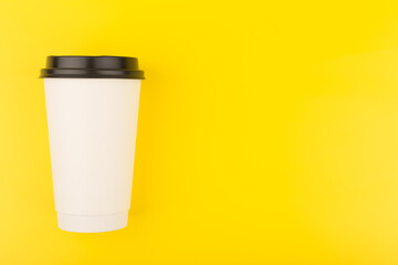 White tall cardboard cup with tea or coffee on bright yellow background with copy space. Concept of hot drinks for take away