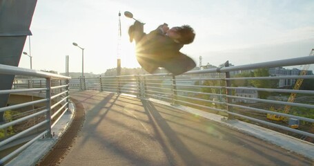 a young businessman looks at his phone, receives good news and jumps for joy scrolling around his axis and raises his hands up in a sign of victory against the backdrop of the sun in the industrial - Powered by Adobe
