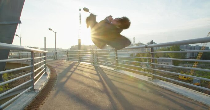 a young businessman looks at his phone, receives good news and jumps for joy scrolling around his axis and raises his hands up in a sign of victory against the backdrop of the sun in the industrial