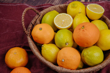 side view of fresh ripe lemons and oranges in a wicker basket on dark red fabric on rustic background