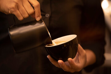Fototapeta na wymiar Close up hand pouring milk in coffee cup to make latte coffee