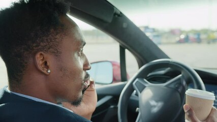 Businessman in stylish suit talking on mobile phone while sitting in luxury car with cup of coffee in hand. African male taking stop during drive for solving working issues. Man talking on mobile - Powered by Adobe