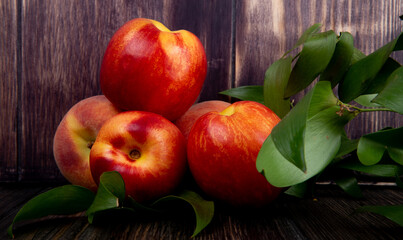 side view of fresh ripe nectarines with green leaves on rustic wooden background