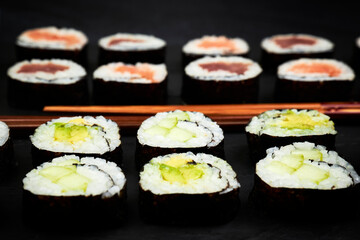 Close-up of a slate of fish sushi and vegetable sushi next to chopsticks. Japanese culture