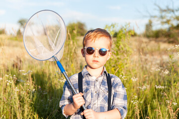 Butterfly hunter - little cute boy wearing sunglass and holding bug net in the hands, standing in...