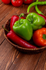 side view of fresh vegetables colorful bell peppers red chili peppers in a wicker basket on wooden rustic background
