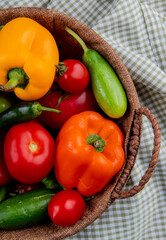 side view of fresh vegetables ripe tomatoes colorful bell peppers green chili peppers and cucumbers in a wicker basket on plaid fabric