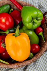 side view of fresh vegetables ripe tomatoes colorful bell peppers green chili peppers in a wicker basket on plaid fabric