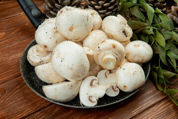 side view of fresh white mushrooms on a frying pan on wooden background