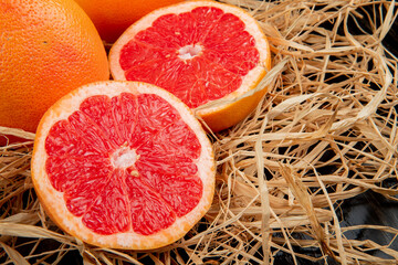 side view of halves of grapefruit on straw on black background