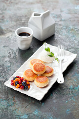 Cottage cheese pancakes, fritters or syrniki served with berries and sour cream on a white plate, selective focus