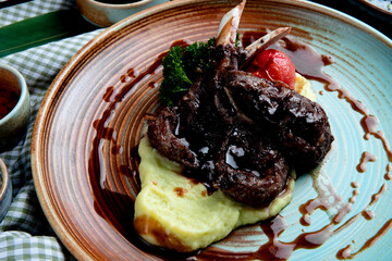 side view of mashed potatoes with roasted lamb chops and vegetables with soy sauce on a plate on wooden background