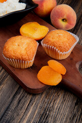 side view of muffins with dried apricots on wooden cutting board and fresh peaches on rustic background