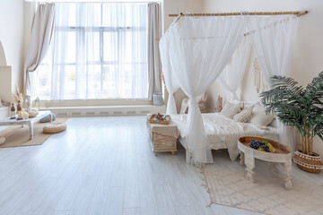 Fototapeta na wymiar daylight through a huge panoramic window illuminates the cozy oriental interior of the room in beige colors with wicker furniture and authentic elements