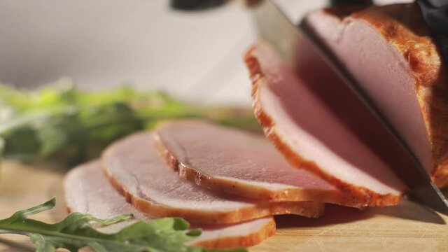 Slicing traditional ham into pieces on a wooden cutting board with a knife. Thin slices of meat. Concept of delicious food snacks and cooking.