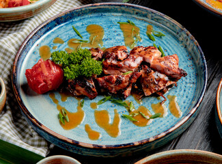 side view of roasted chicken with grilled tomato fresh herbs and sauce on a plate on wooden background