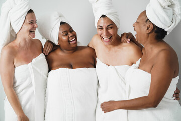 Multigeneration women with diverse skin and body laughing together while wearing body towels -...
