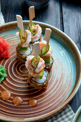 side view of set of baked sushi rolls with shrimps served with wasabi and ginger on a plate on wooden background