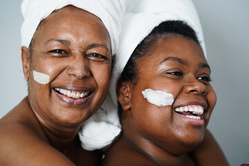African mother and daughter doing beauty treatment at home using skin mask - Body care and family...