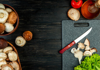side view of sliced and whole mushrooms with kitchen knife on a black cutting board on black wooden background with copy space