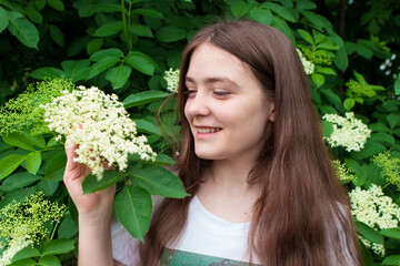 Beautiful girl 13 years old with long hair and an elder tree. Summer bloom in June, human unity with nature or natural hair care with plants.