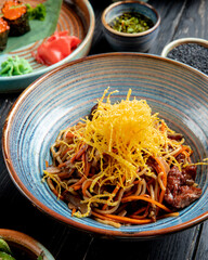 side view of stir fried noodles with beef and vegetables in a plate on wooden table