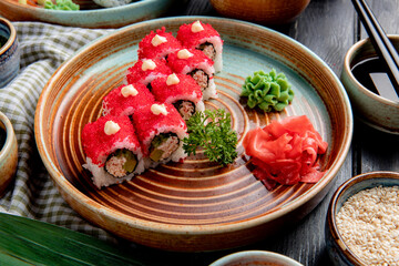 side view of sushi roll with crab avocado covered with red caviar with ginger and wasabi on a plate on wooden background
