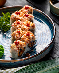 side view of sushi rolls with rice shrimp tempura avocado and cheese inside on a plate with ginger and wasabi on wooden background
