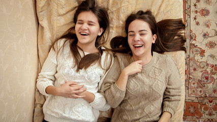 Two happy laughing girls relaxing on bed and talking. Teenager friendship and relationship