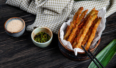 side view of tempura vegetables in a bowl served with soy sauce on wooden background with plaid fabric
