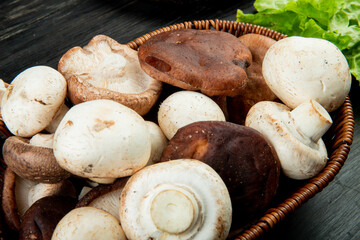 side view of various types of fresh mushrooms in a wicker basket on dark rustic wooden background
