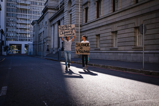 Two mixed race male friends carrying hand painted protest signs walking in city street