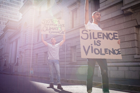 Two mixed race male friends carrying protest signs with slogans in sunny city street