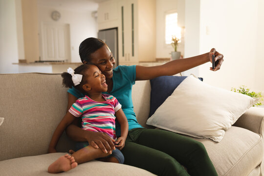 Happy african american mother and daughter relaxing on couch and taking selfie