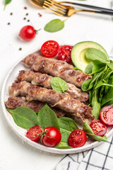 Ketogenic diet, grilled sausages minced meat wrapped in bacon with with spinach, avocado and cherry tomato. chevapchichi or Kofta kebab, Keto paleo diet menu