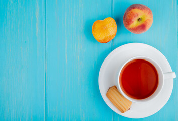 top view of a cup of tea with biscuit and fresh ripe peaches on blue background with copy space
