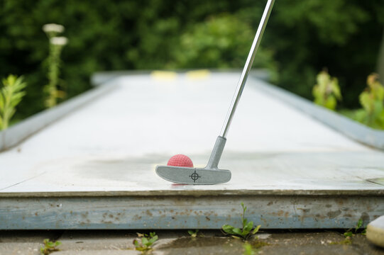 Close-up Of Playing Mini Golf. Red Ball And Stick. Summer Outdoor Game.