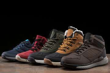 five winter boots of different colors, stand in a row, one after the other, on a black background,...